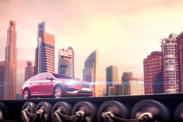 red-car-driving-with-headlights-on-with-city-skyline